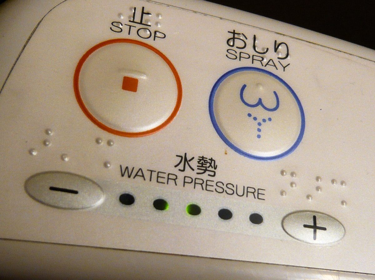 Close-up of a bidet toilet seat control with a red stop button and a blue spray button