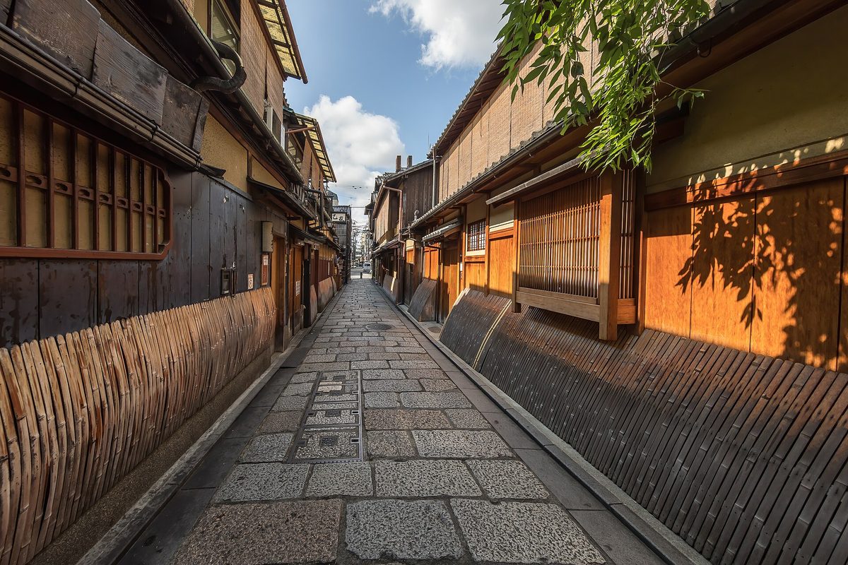 An empty stone-paved lane between wooden houses with bamboo blinds