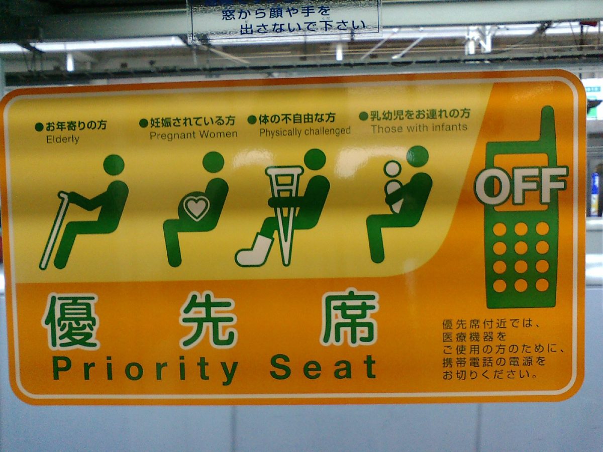 An older priority seat sign on a Japanese train, with pictograms for older people, pregnant women, people with physical challenges and people with infants, and a mobile phone marked OFF