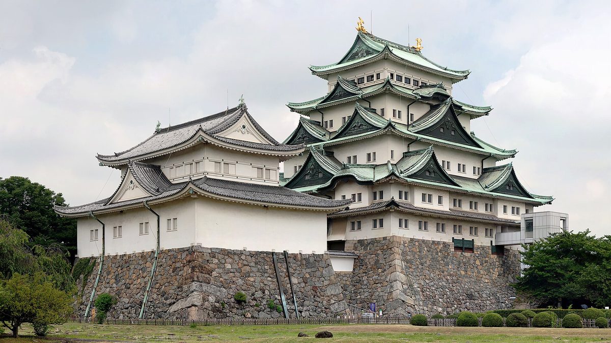 The white main keep of Nagoya Castle with green roofs on a stone base