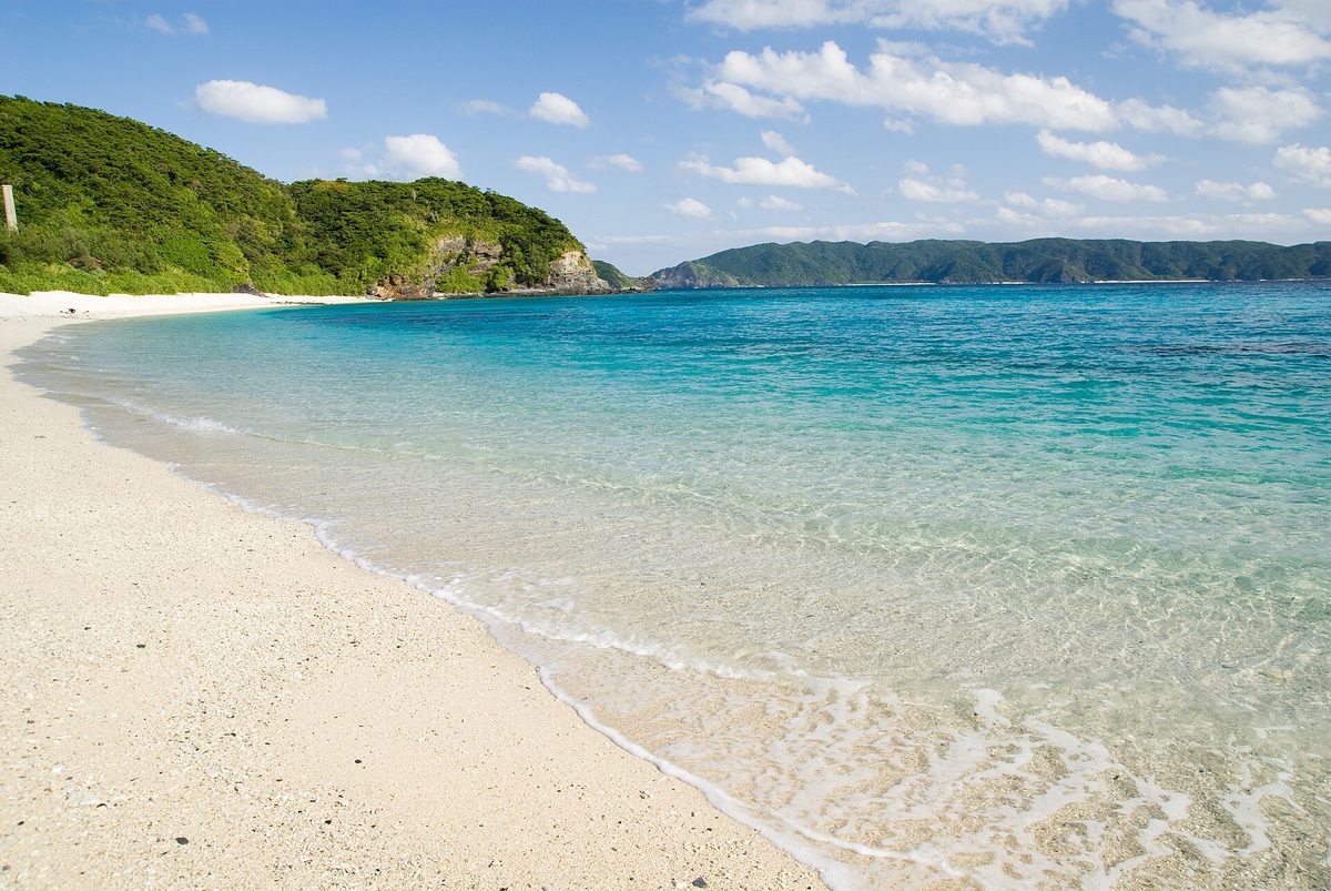 A white sand beach with clear turquoise water and green hills