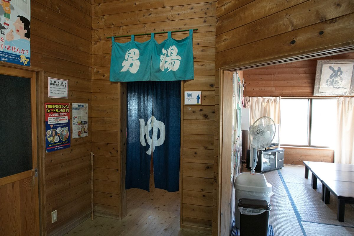 A blue noren curtain marked for the men's bath in a wooden changing area